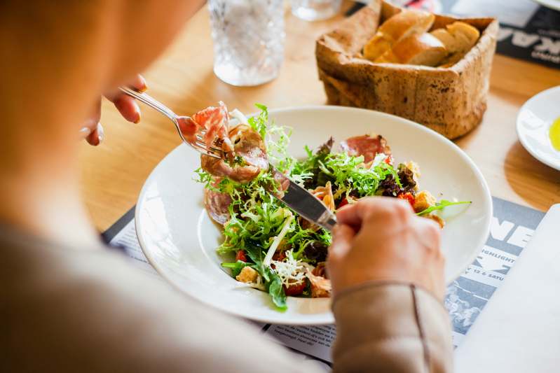 Warm kitchen photo: smiling parent and child stirring a colorful pasta dish together, measuring spoons and fresh veggies visible on counter
